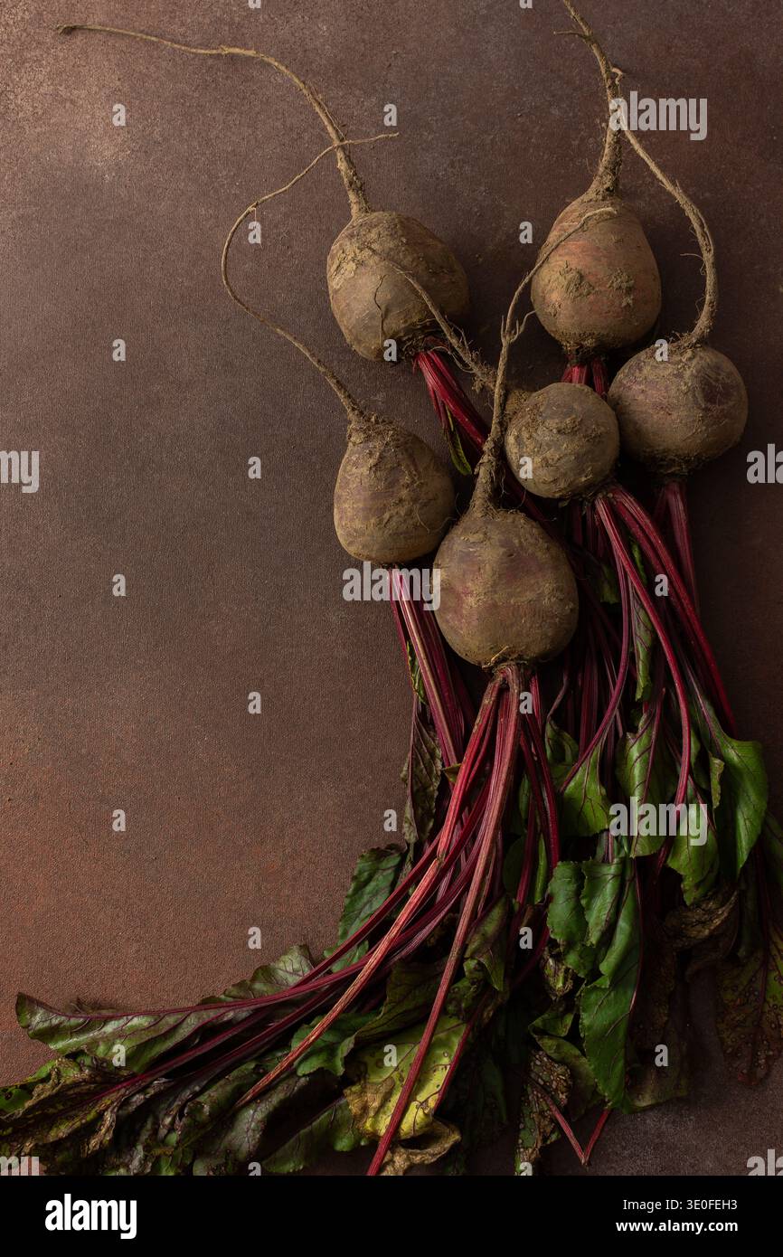 Rüben mit grünen Blättern ruhen auf einer braunen Oberfläche in einer Küche. Die Umgebung ist warm und gibt Hinweise auf frische Produkte, die zum Kochen oder Essen bereit sind Stockfoto