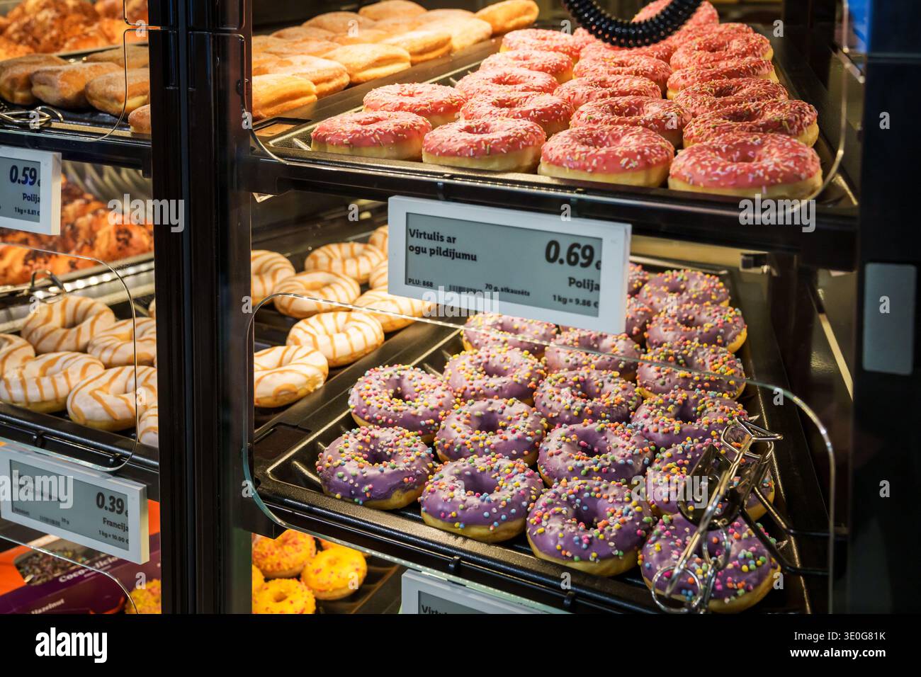 RIGA, LETTLAND. März 2026. Eine bunte Auswahl glasierter Donuts mit Streuseln und Füllungen in einem Supermarkt-Bäckereietui. Neue LIDL-Filialöffnung. Stockfoto