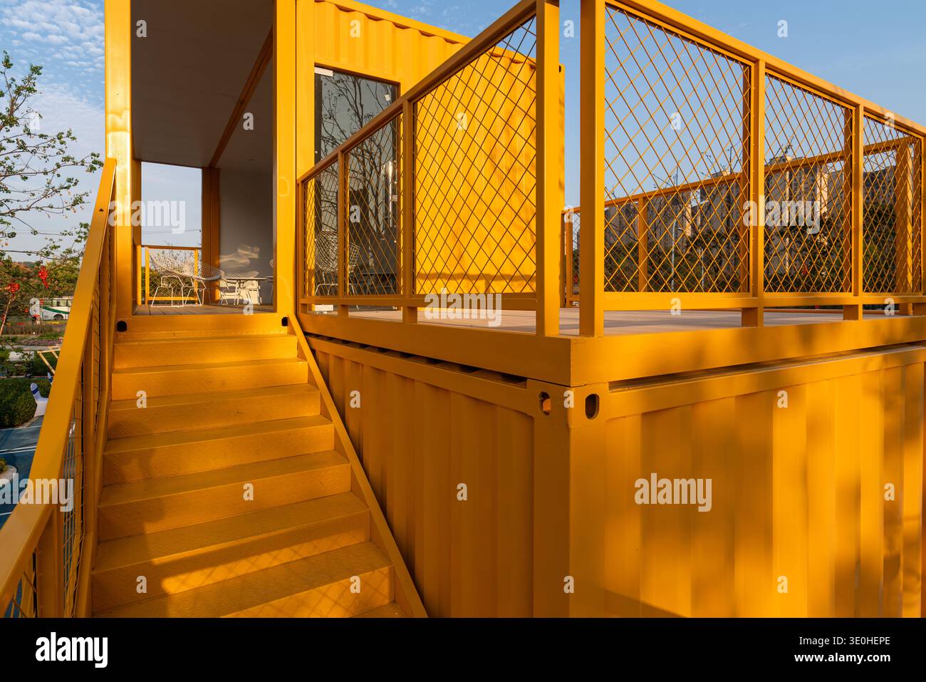 Beschreibung: Eine gelbe moderne Plattform im Containerstil mit Geländern in einem Stadtpark. Das Bild vermittelt urbane Architektur, modernes Design und Outdoor-e Stockfoto