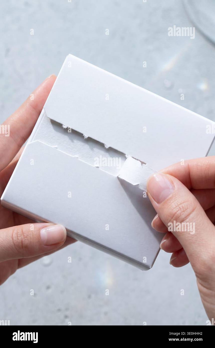 Modell einer weißen quadratischen Schachtel mit einer Tränenstreiföffnung, gehalten von Händen. Stockfoto