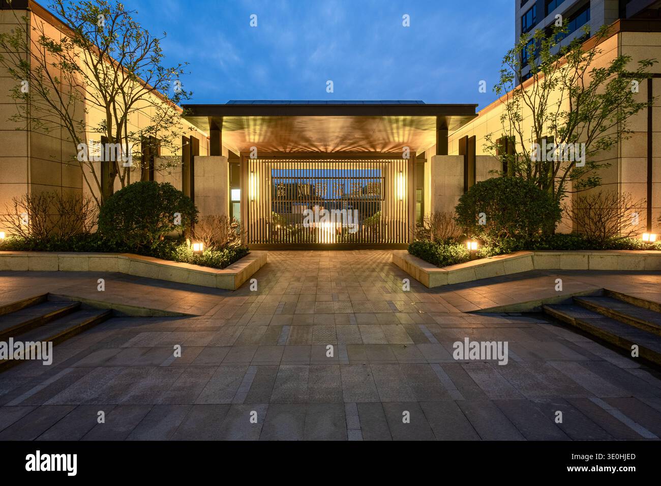 Beschreibung: Ein weiter Blick auf einen strukturierten Innenhof und Gartenbereich in einem luxuriösen Wohngebiet bei Nacht. Das Bild vermittelt Architekturdesign und Stockfoto