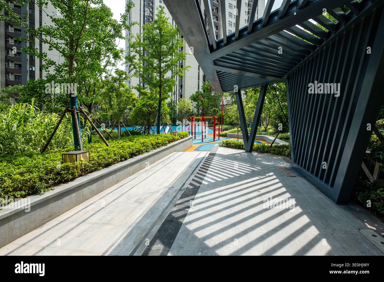 Beschreibung: Eine moderne Pergola, die dynamische Licht- und Schattenmuster auf einem Parksteg erzeugt. Das Bild vermittelt Designdetails, Architektur und Atmosphäre Stockfoto