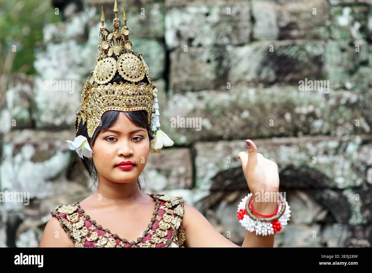 Eine junge Frau tanzt in traditionellen kambodschanischen Kleidern mit einer goldenen Krone vor einem antiken Tempel in Kambodscha. Stockfoto