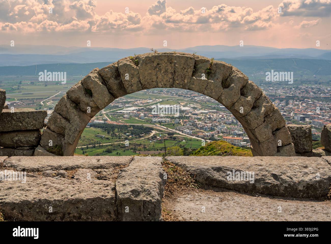 Der alte Steinbogen von Pergamon-Ruinen umrahmt Bergama Stadt, Tal und ferne Berge unter einem bewölkten Himmel, Izmir, Türkei Stockfoto