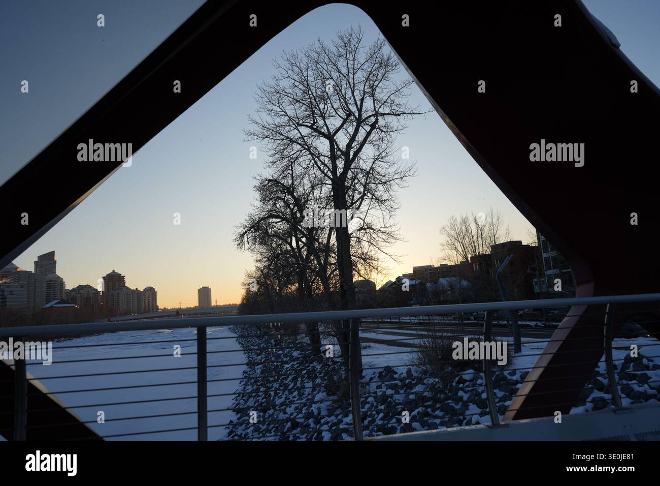 Winterblick auf die berühmte, moderne rote Friedensbrücke, entworfen von Santiago Calatrava, überquert den gefrorenen Bow River bei Sonnenuntergang in der Innenstadt von Calgary Stockfoto
