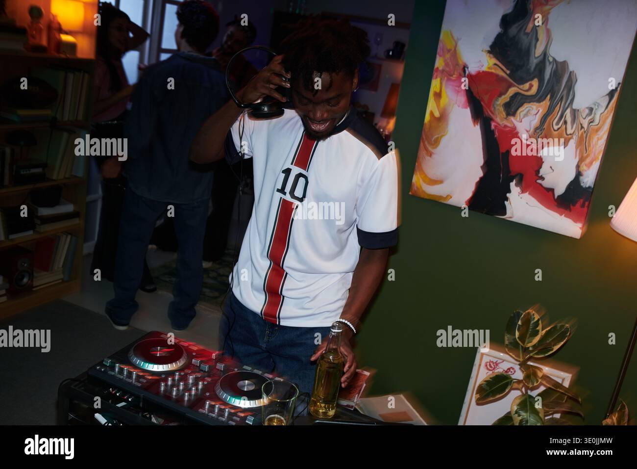 Young Black man DJing auf Party mit Freunden, die im Hintergrund gesellig sind Stockfoto