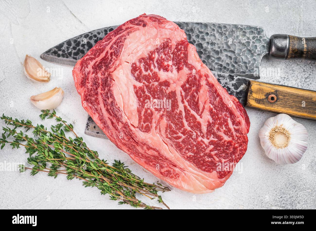 Hochwertiges rohes Ribeye-Rindersteak mit intensiver Marmorierung und dicker Fettkappe. Rustikaler Metzgerstil auf hellem Steinhintergrund. Stockfoto