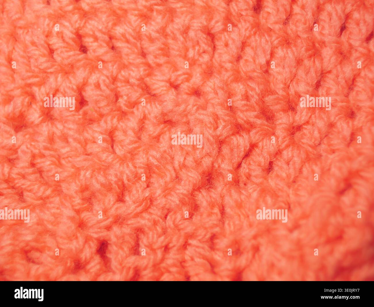 Eine hochauflösende Makroaufnahme eines pfirsichfarbenen oder korallenfarbenen Strickstoffs. Das Bild fängt die komplizierten Schlaufen und weichen Fasern des Garns ein und betont Stockfoto