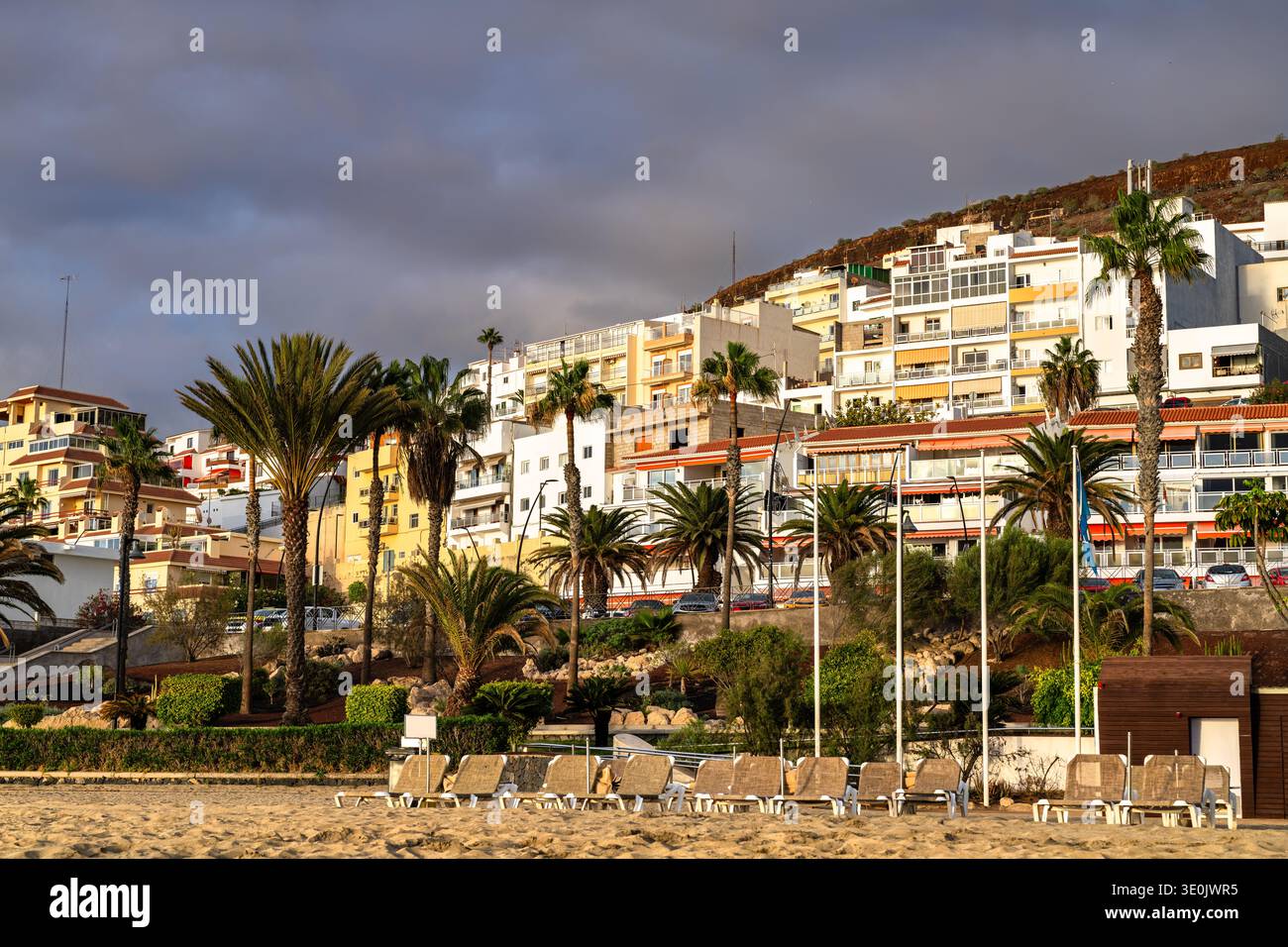 Malerischer Blick auf den Strand Playa de Las Vistas mit Liegestühlen, Palmen und Hotels, die sich entlang der Küste unter bewölktem Himmel erheben. Stockfoto
