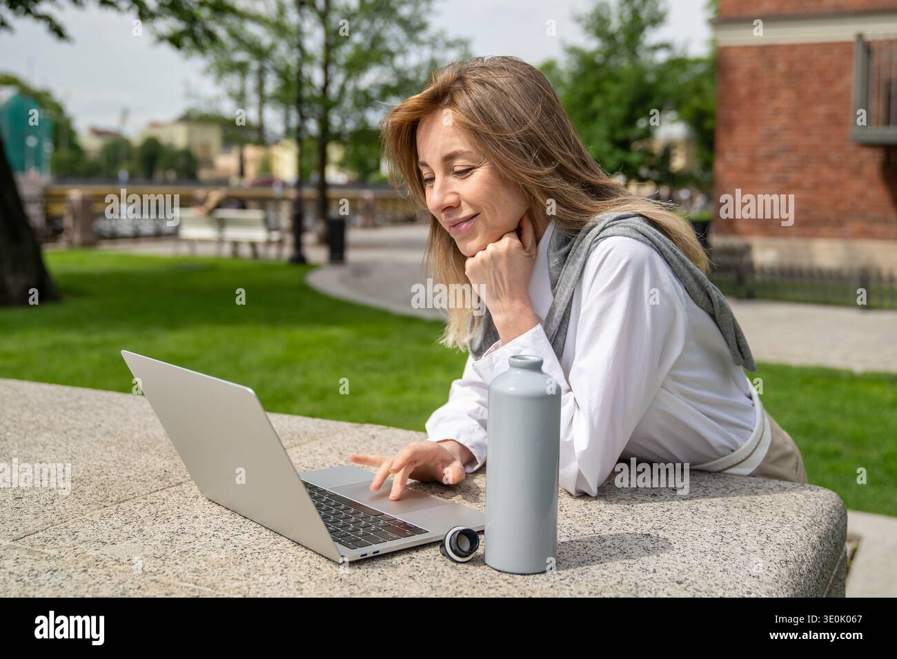 Lächelnde, glückliche Geschäftsfrau arbeitet am Sommertag gern im Freien an einem Laptop, was die Vorteile der Fernarbeit ist Stockfoto