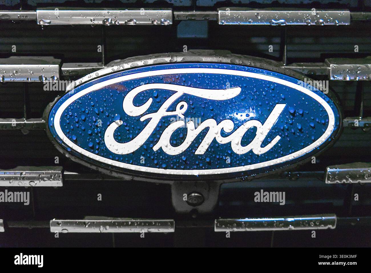 Nahaufnahme eines feuchten Ford-Logos mit Wassertropfen auf blauer Oberfläche. Stockfoto