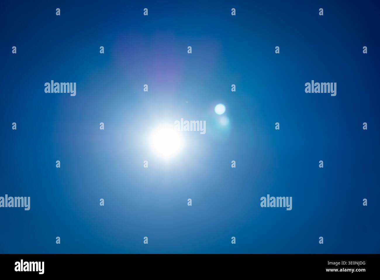 Helle Sonne, die an einem klaren blauen Himmel mit sichtbarem Halos- und Linsenlicht leuchtet. Stockfoto