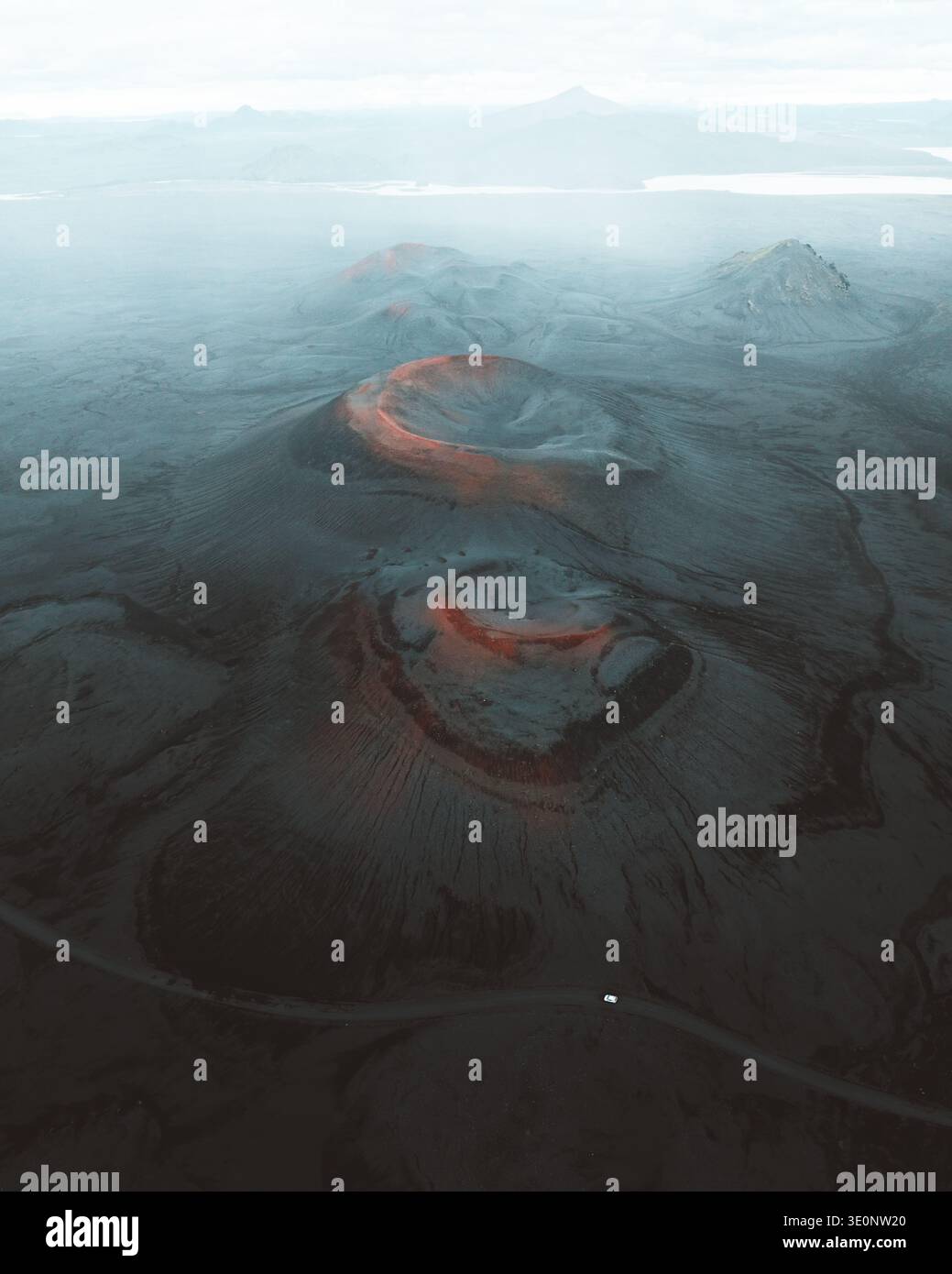 Aus der Vogelperspektive auf den starken Kontrast zwischen dem dunklen, vulkanischen Gelände und den leuchtenden roten Kratern, die eine surreale Landschaft schaffen, Rangárþing ytra, Island Stockfoto