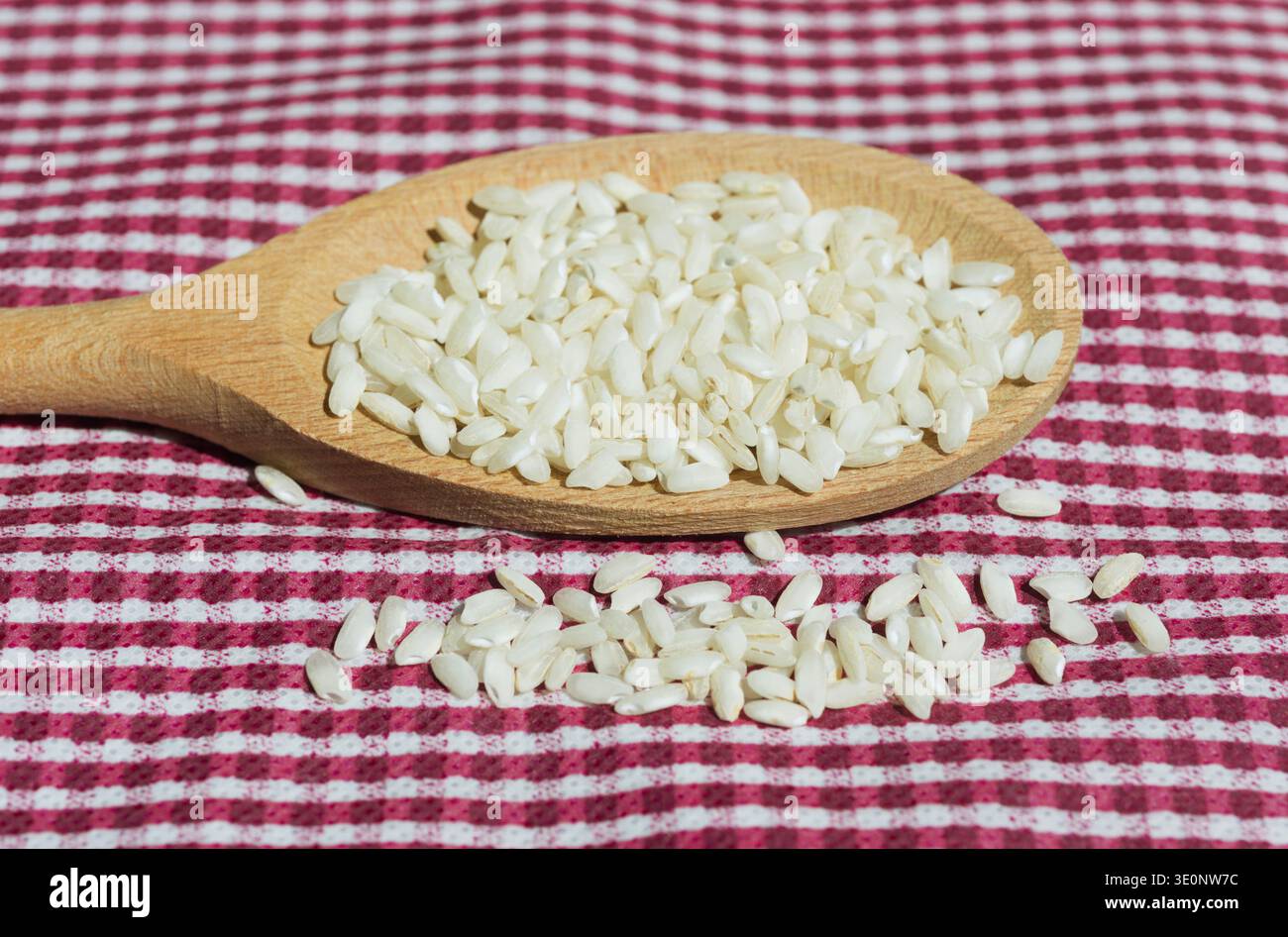 Holzlöffel mit weißem Reis auf karierter Tischdecke Stockfoto