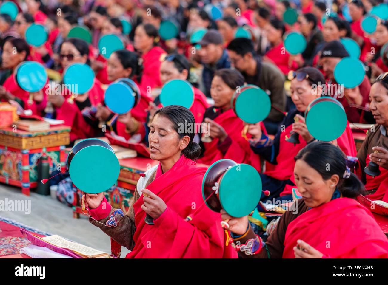 Frauen in traditioneller roter Kleidung spielen zeremonielle Handtrommeln und Glocken während einer religiösen Versammlung im Dorf Panamik. Stockfoto