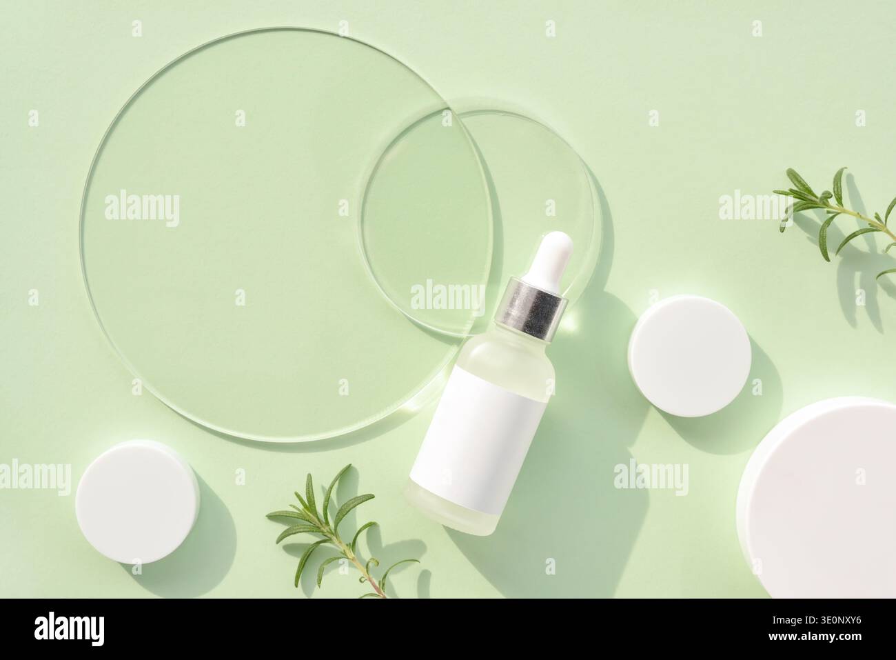 Frischer mintgrüner Hintergrund mit Serumtropfflasche und transparenten Glasscheiben, Cremegläsern und Rosmarinzweig. Spa-Konzept. Draufsicht mit s Stockfoto