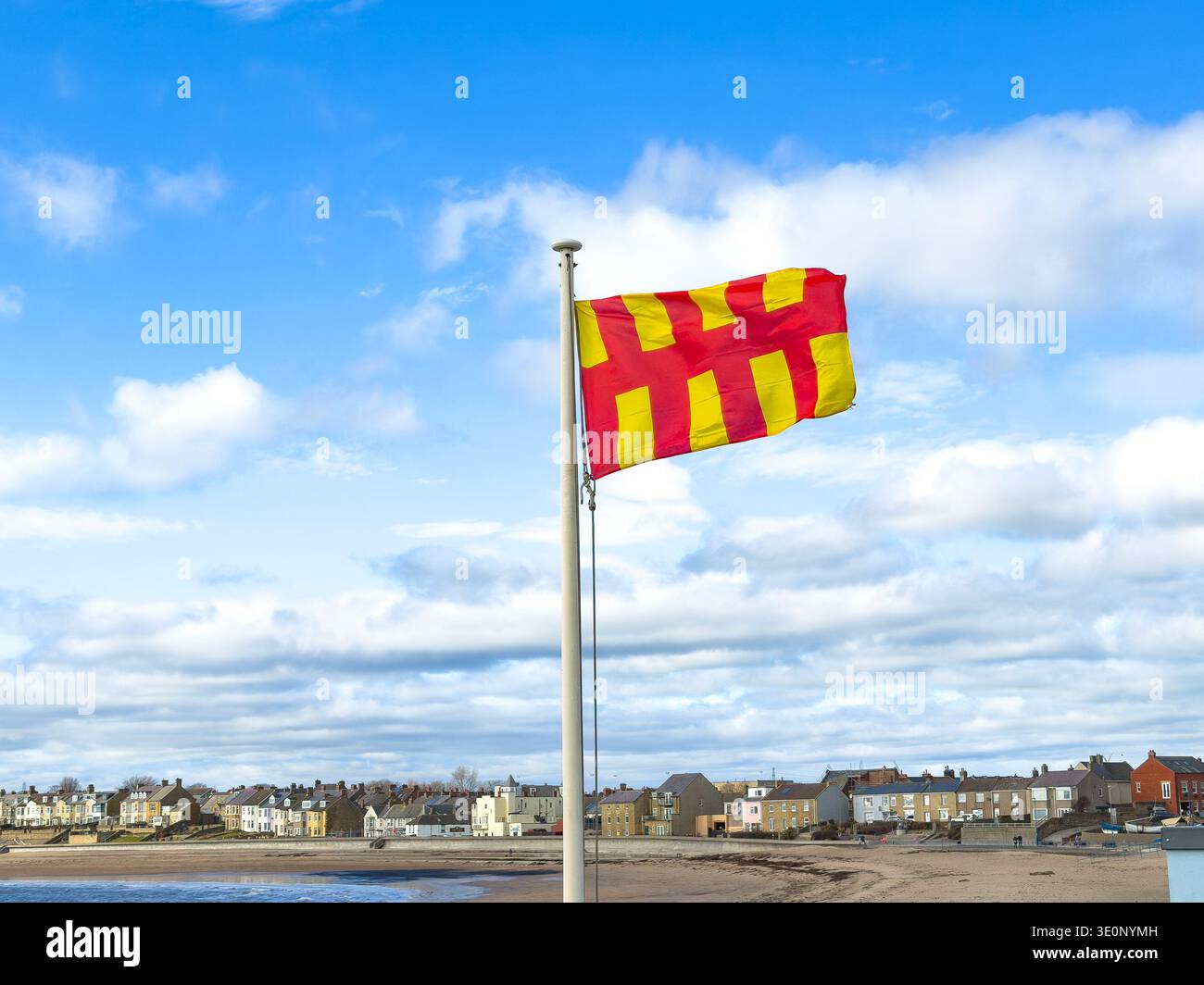 Küstenszene mit roter und gelber Northumberland-Flagge, die am Pol fliegt und den sandigen Strand überblickt, ruhiges Wasser der Newbiggin Bay northumberland uk - Smartphone-aufgenommenes Stockfoto