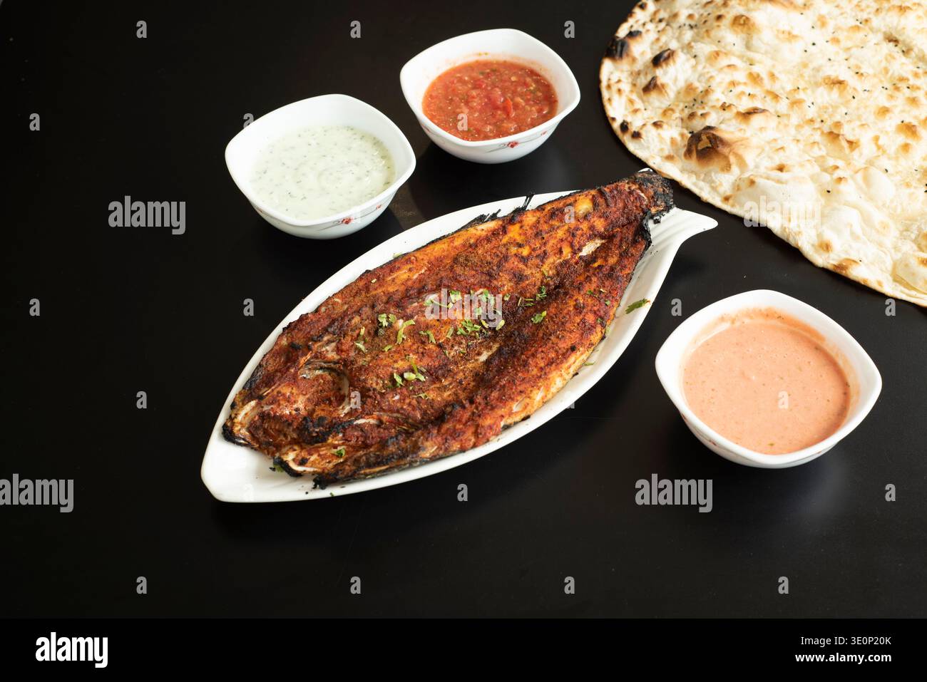 Köstlicher gegrillter Fisch im arabischen Stil, serviert mit Fladenbrot und einer Auswahl an Dips und Saucen Stockfoto
