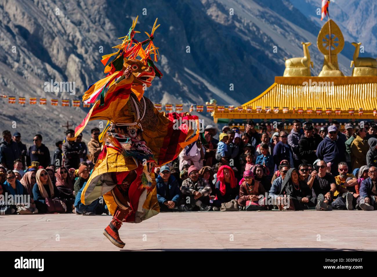 Eine Darstellerin in Hirschmaske und bunten Seidengewändern tanzt beim Diskit Gustor Festival mit einem goldenen Schrein in der Ferne. Bezirk Leh UN Stockfoto