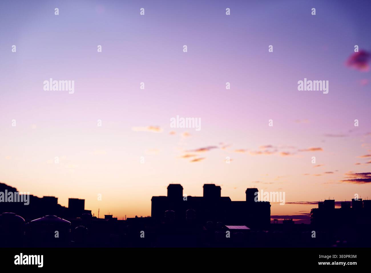 Traumhafter Sonnenuntergang in Taiwan mit violett-rosa Himmel, verstreuten Wolken und dunklen Silhouetten von Gebäuden und Türmen am Horizont. Stockfoto