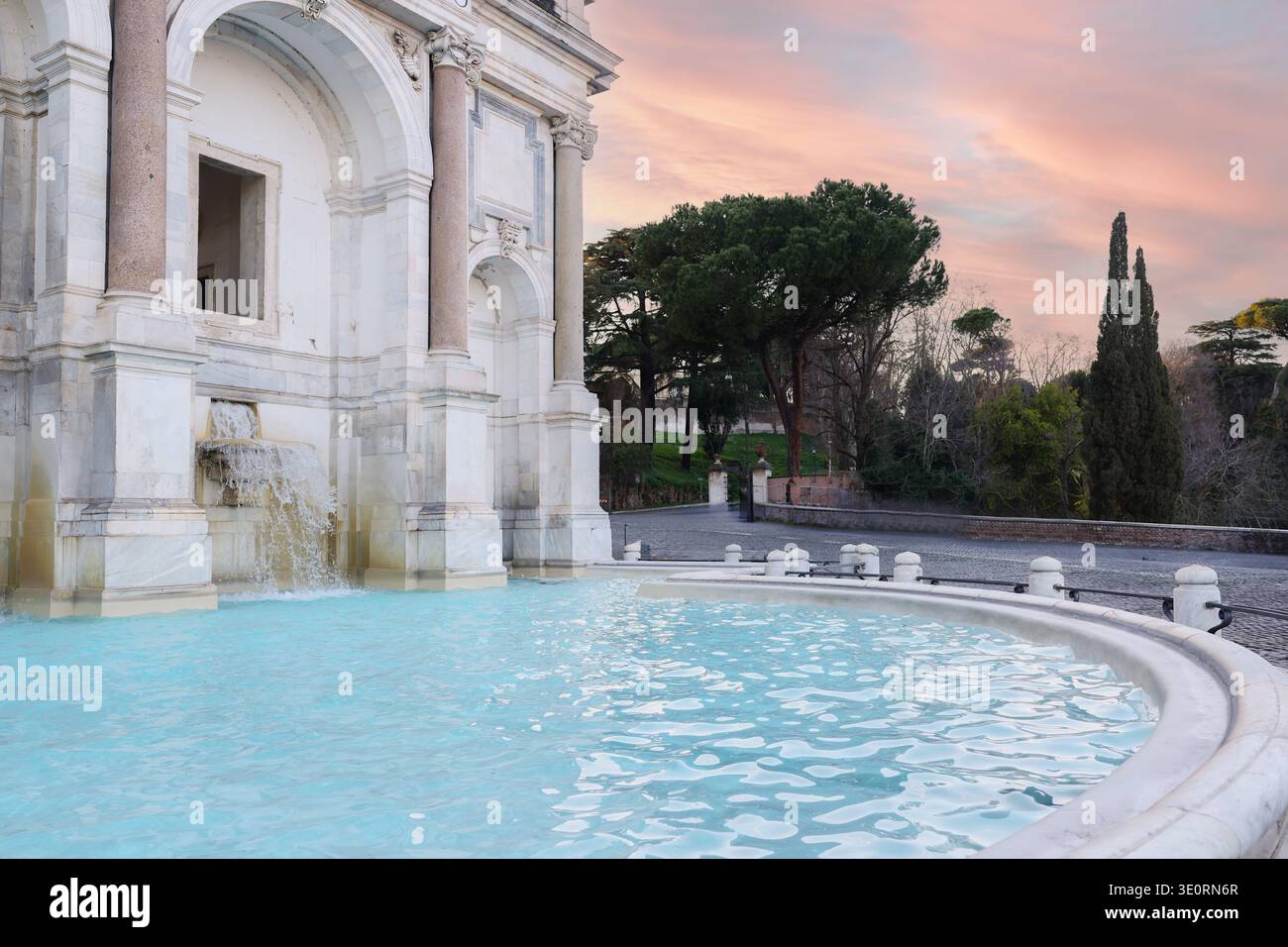 Historischer Brunnen mit türkisfarbenem Wasser in der Nähe klassischer Architektur im Park Rom bei Sonnenuntergang. Friedliches europäisches Reiseziel. Stockfoto