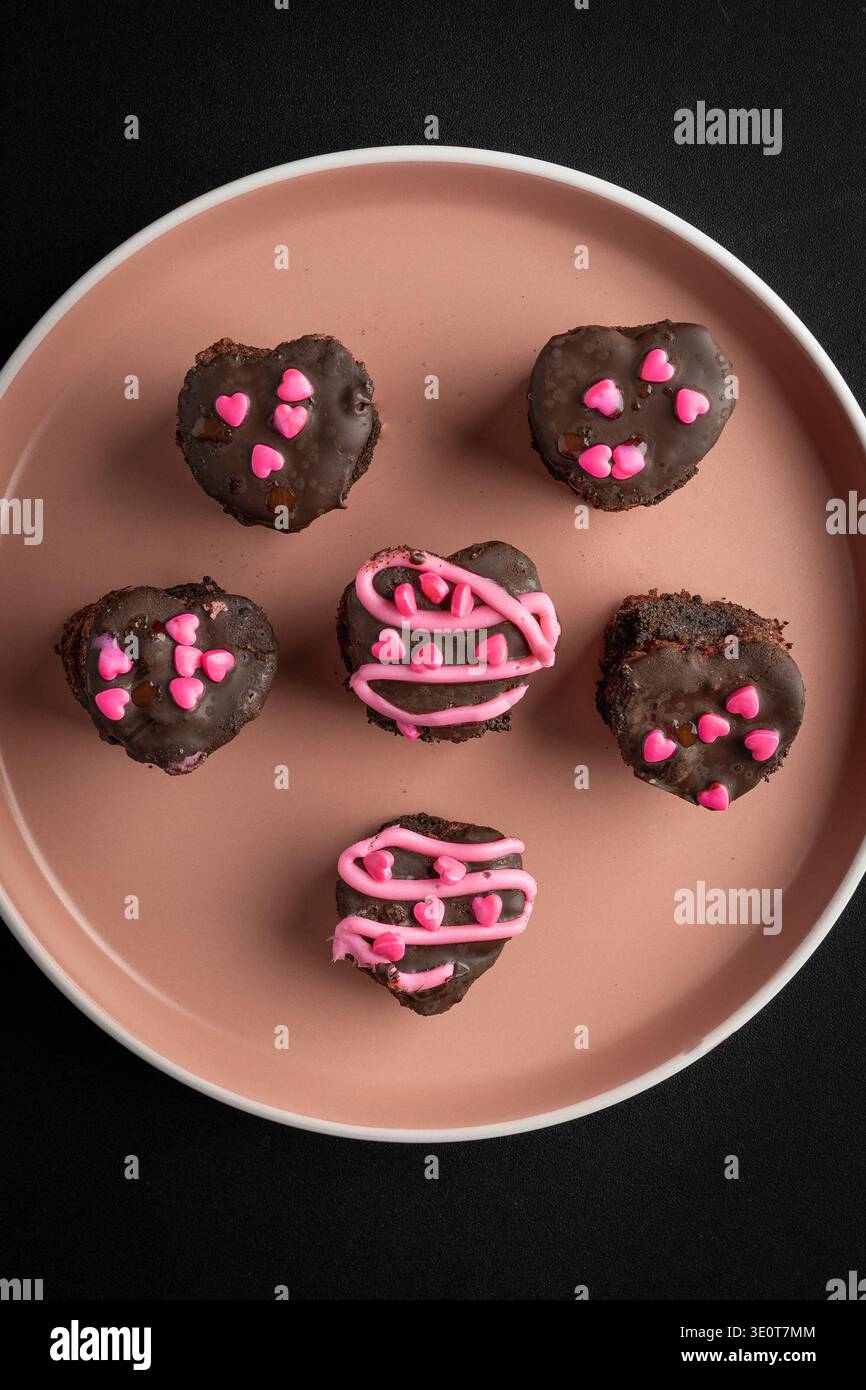 Schokoladenherz-Desserts mit rosa Sprinkles auf minimalistischem Teller Stockfoto