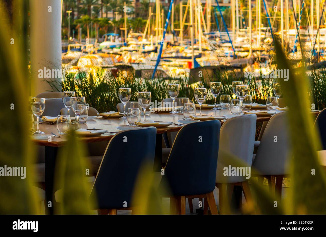 Eleganter Esstisch im Freien mit Blick auf einen sonnigen Hafen mit Segelbooten Stockfoto