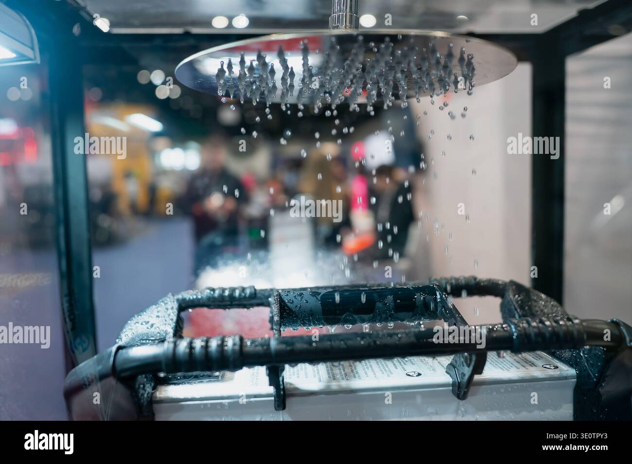 Wasserspritzung von einer Deckendüse auf eine Geräteeinheit mit oberem Griff während einer Live-Produktvorführung im Innenbereich auf einer Messe Stockfoto