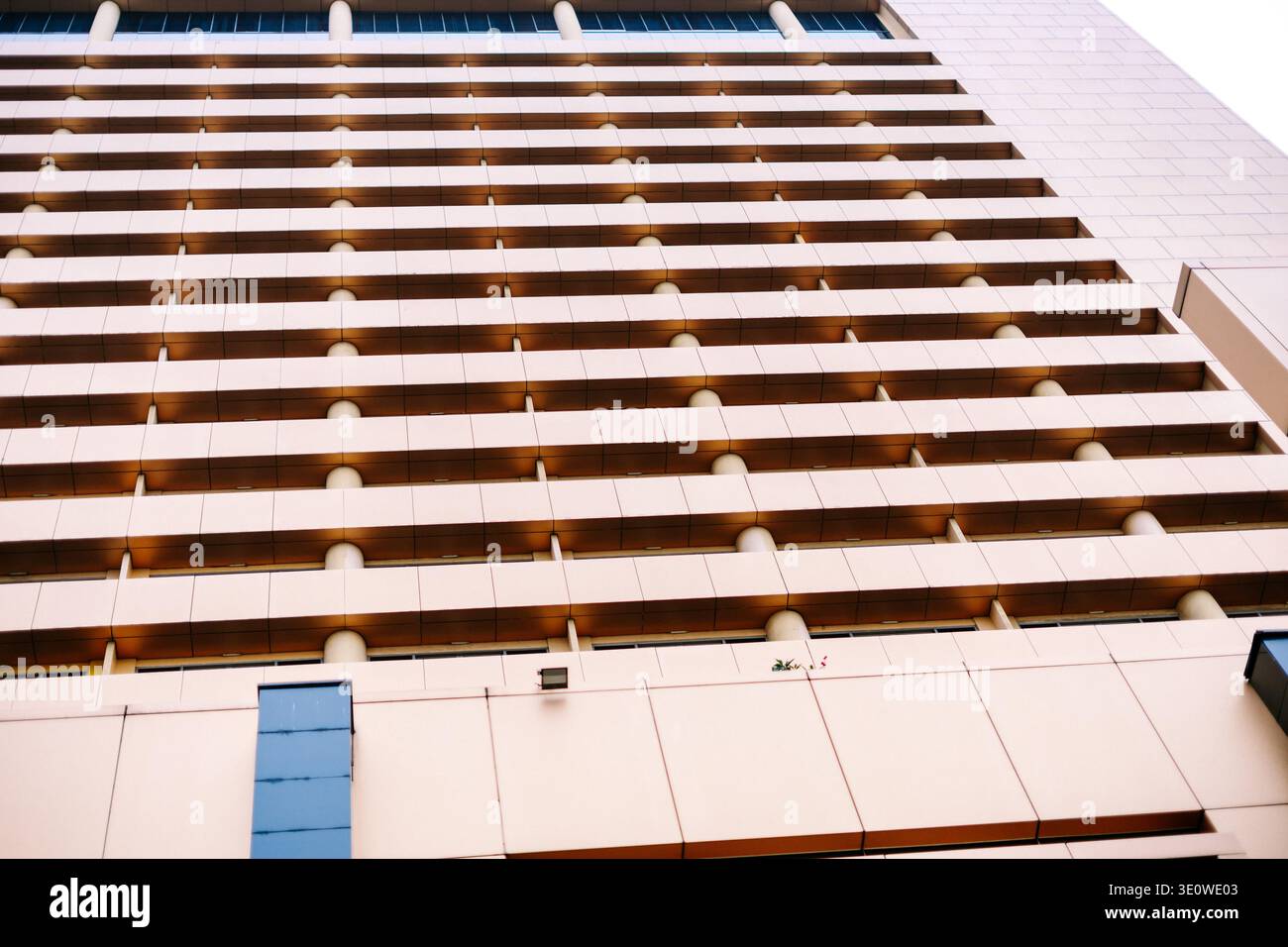 Blick von unten auf eine moderne Gebäudefassade mit geometrischen Mustern mit beigefarbenen Paneelen, sich wiederholenden horizontalen Elementen und dezenten Fenstern, kreativ Stockfoto