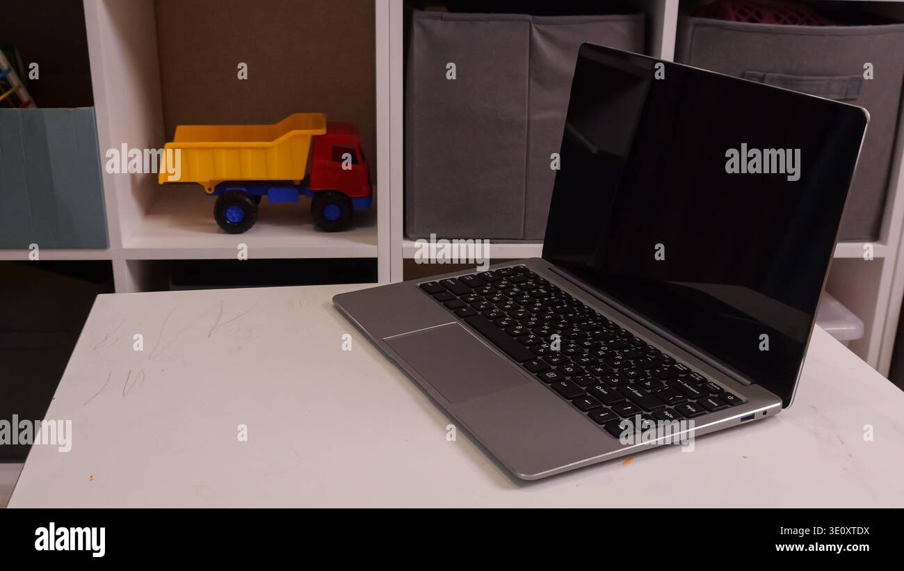 Laptop In Der Nähe Des Spielzeugwagens Auf Dem Tisch, Eltern Verwalten Haushaltsaufgaben Aus Der Ferne, Telefon Und Planer In Der Nähe, Regale Mit Kinderspielzeug Im Hintergrund, Warm Stockfoto