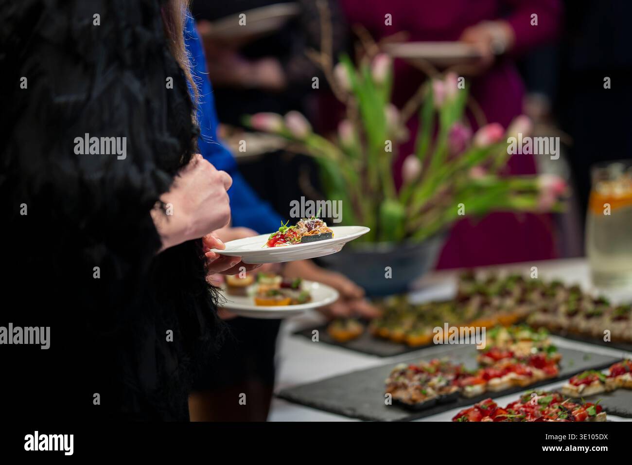 Gäste genießen Gourmet-Canapés an einem eleganten Catering-Buffet während eines Firmenempfangs. Die Leute servieren sich selbst feine Vorspeisen. Stockfoto