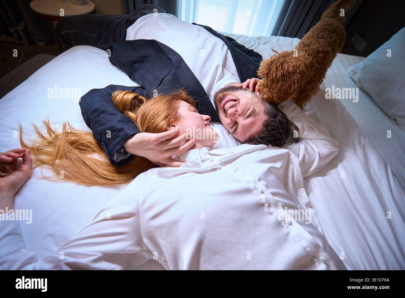 Glückliches junges Paar, das tagsüber im gemütlichen Schlafzimmer mit Hund spielt Stockfoto