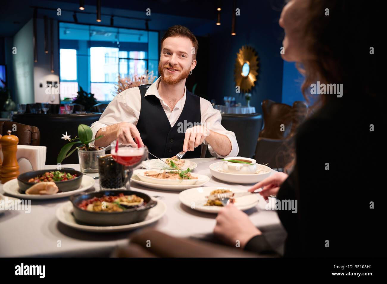 Ein lächelnder Mann, der abends mit einer Frau in einem gemütlichen Restaurant isst Stockfoto
