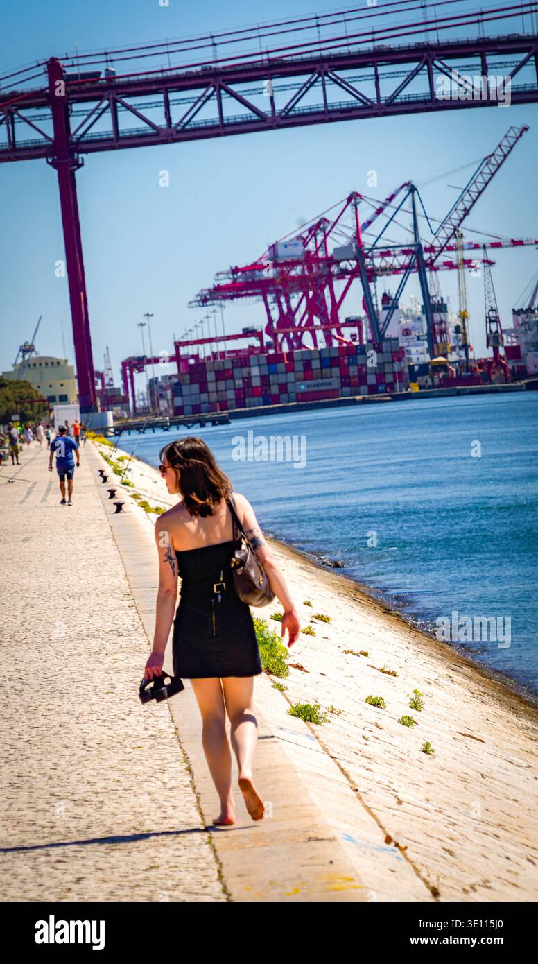Frau am Hafen von Lissabon, die an Hafenkränen und Brücke vorbeiläuft, kühle Industriemusik in Alcantara Lissabon Portugal Stockfoto