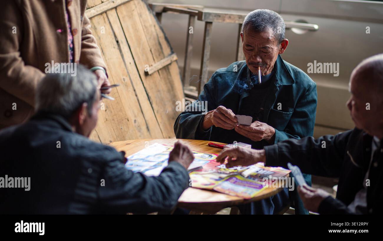 Ältere chinesische Männer spielen Karten und rauchen am runden Tisch im Dorf Longsheng, China Stockfoto