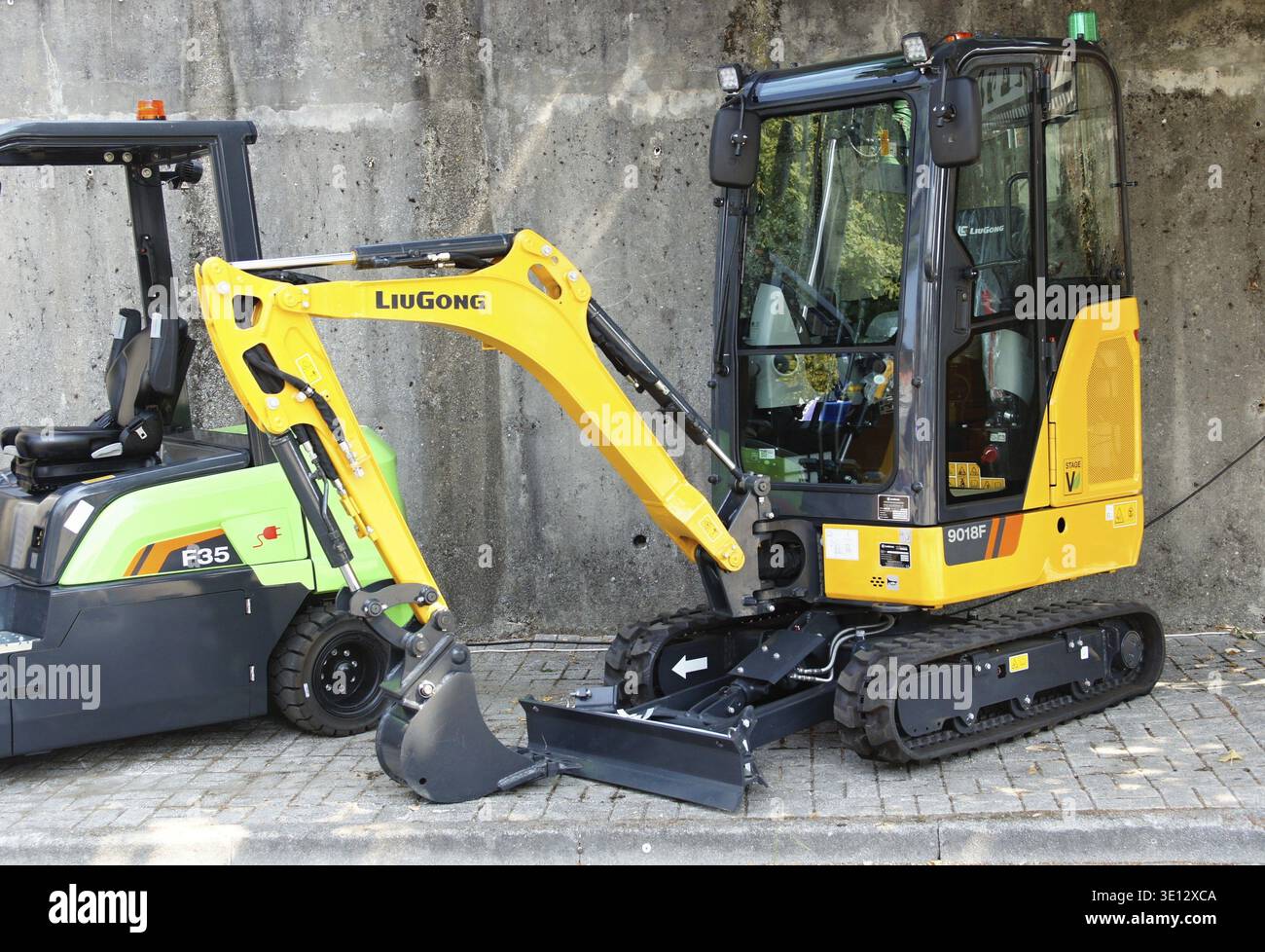 Liugong Minibagger parkt neben einem grünen Elektrostapler F35 auf einem gepflasterten Untergrund Stockfoto