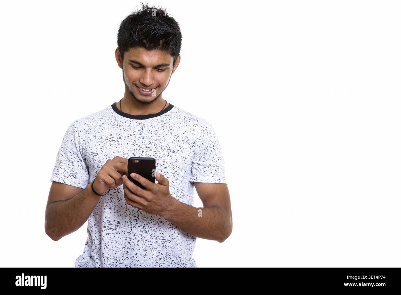 Studio shot junger indischer Mann glücklich lächelnd, während mit Handy Stockfoto