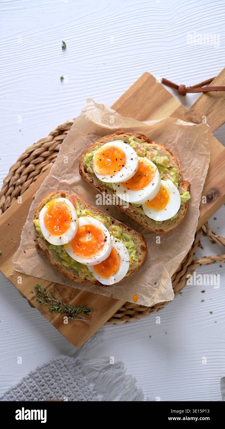 Zwei knusprige Brotscheiben mit cremiger Avocado und lebendig weich gekochten Eiern auf Pergamentpapier. Aufnahmen aus einem hohen Winkel mit hellem, natürlichem Licht Stockfoto
