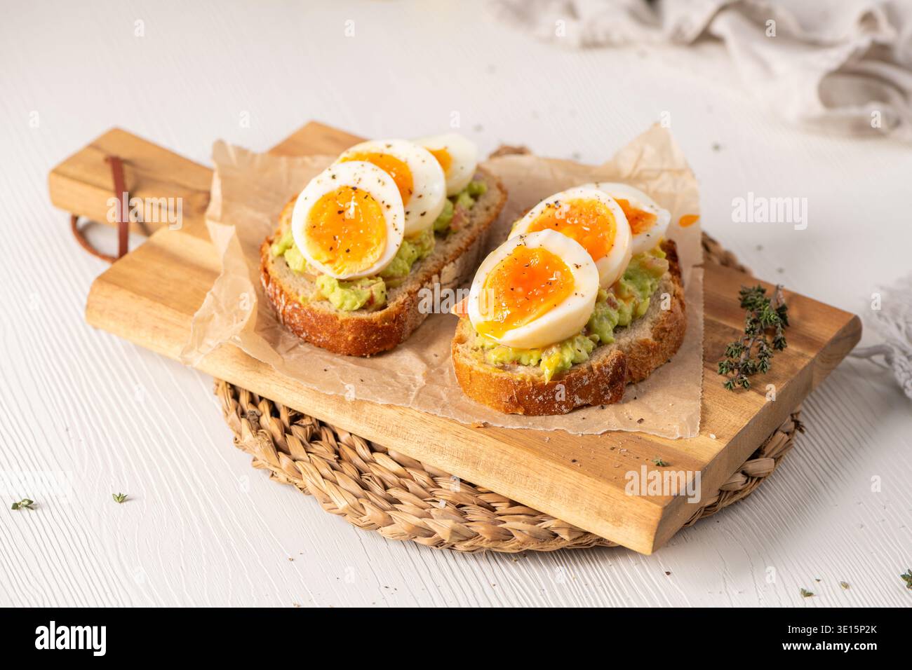 Zwei Scheiben knuspriger Sauerteig mit cremigem Avocadopüree und marmelierten mittelgekochten Eiern. Sanftes Tageslicht unterstreicht die rustikalen Texturen des Th Stockfoto