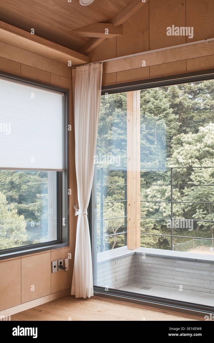 Sitzbank mit Holzfenster und Blick auf die Bäume in ruhiger Inneneinrichtung. Stockfoto
