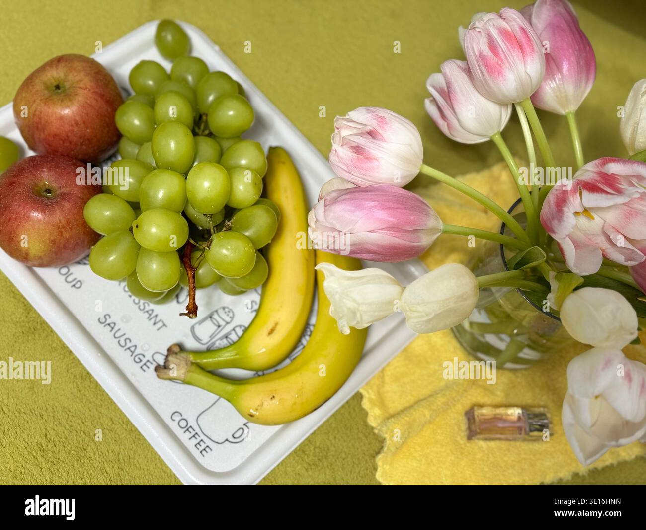 Tablett mit frischem Obst und grünen Trauben, Apfel, Bananen und Tulpenstrauß - Smartphone-aufgenommenes Stockfoto
