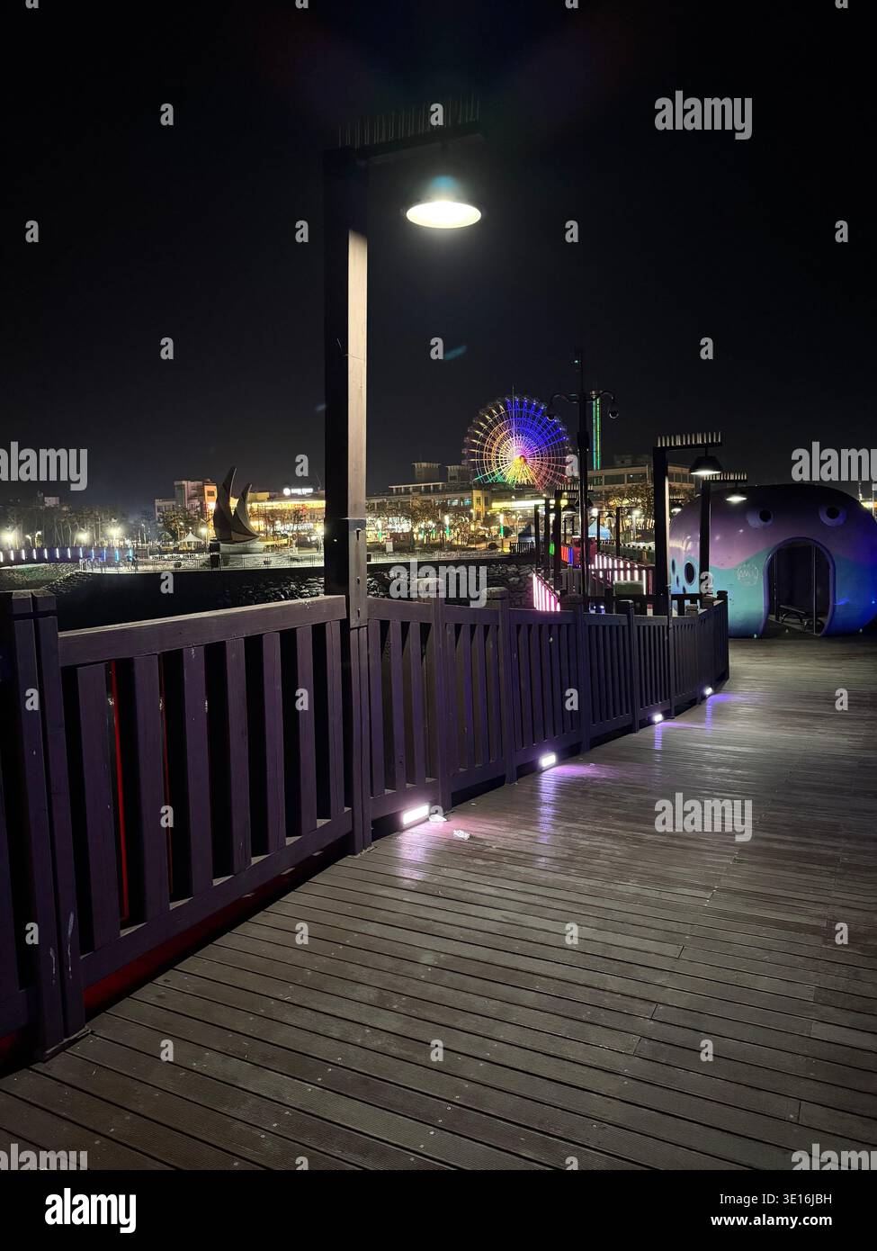 Nachtpromenade mit Riesenrad und farbenfrohen Lichtern am Meer in Südkorea - Smartphone-aufgenommenes Stockfoto