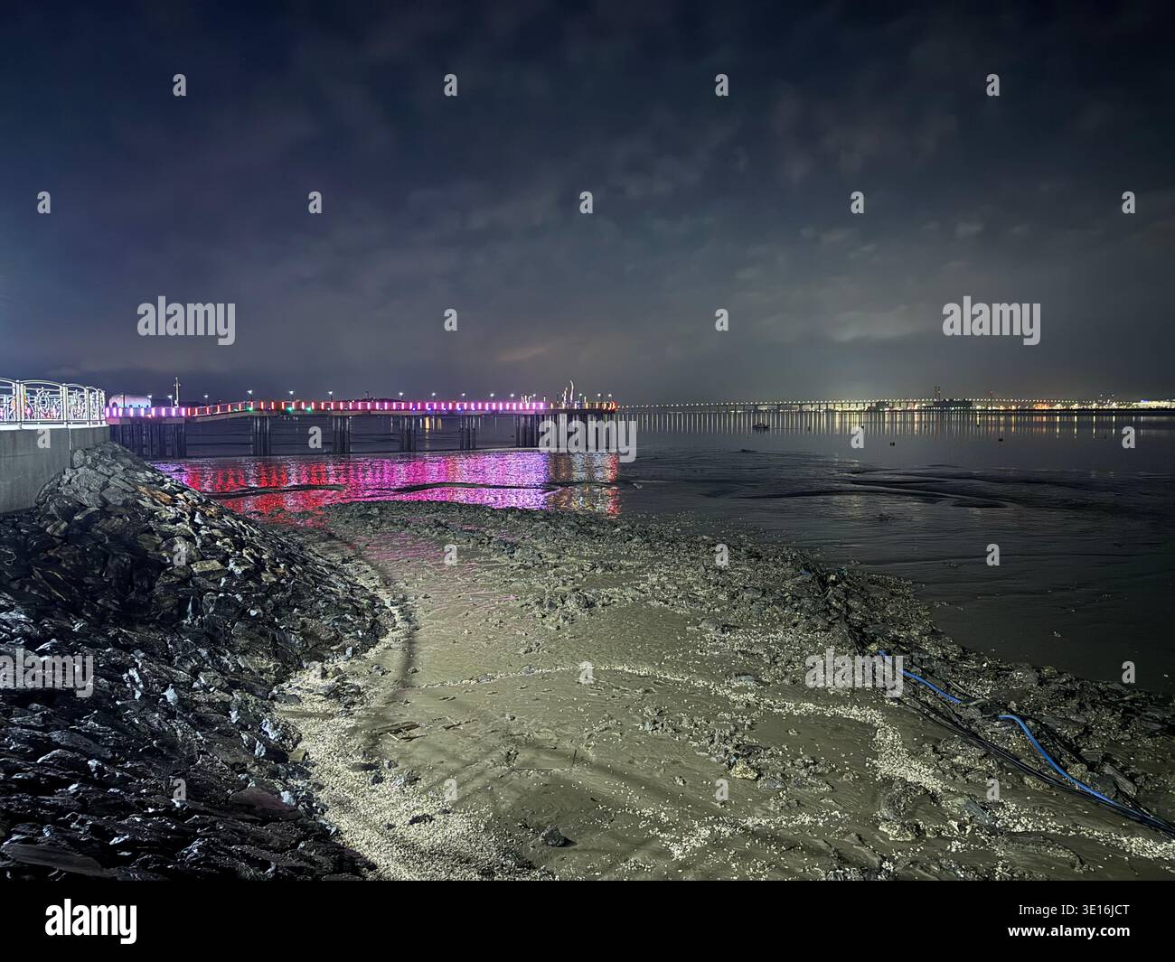 Leuchtender beleuchteter Pier bei Nacht mit bunten LED-Lichtern, die an der südkoreanischen Küste reflektiert werden - Smartphone-aufgenommenes Stockfoto
