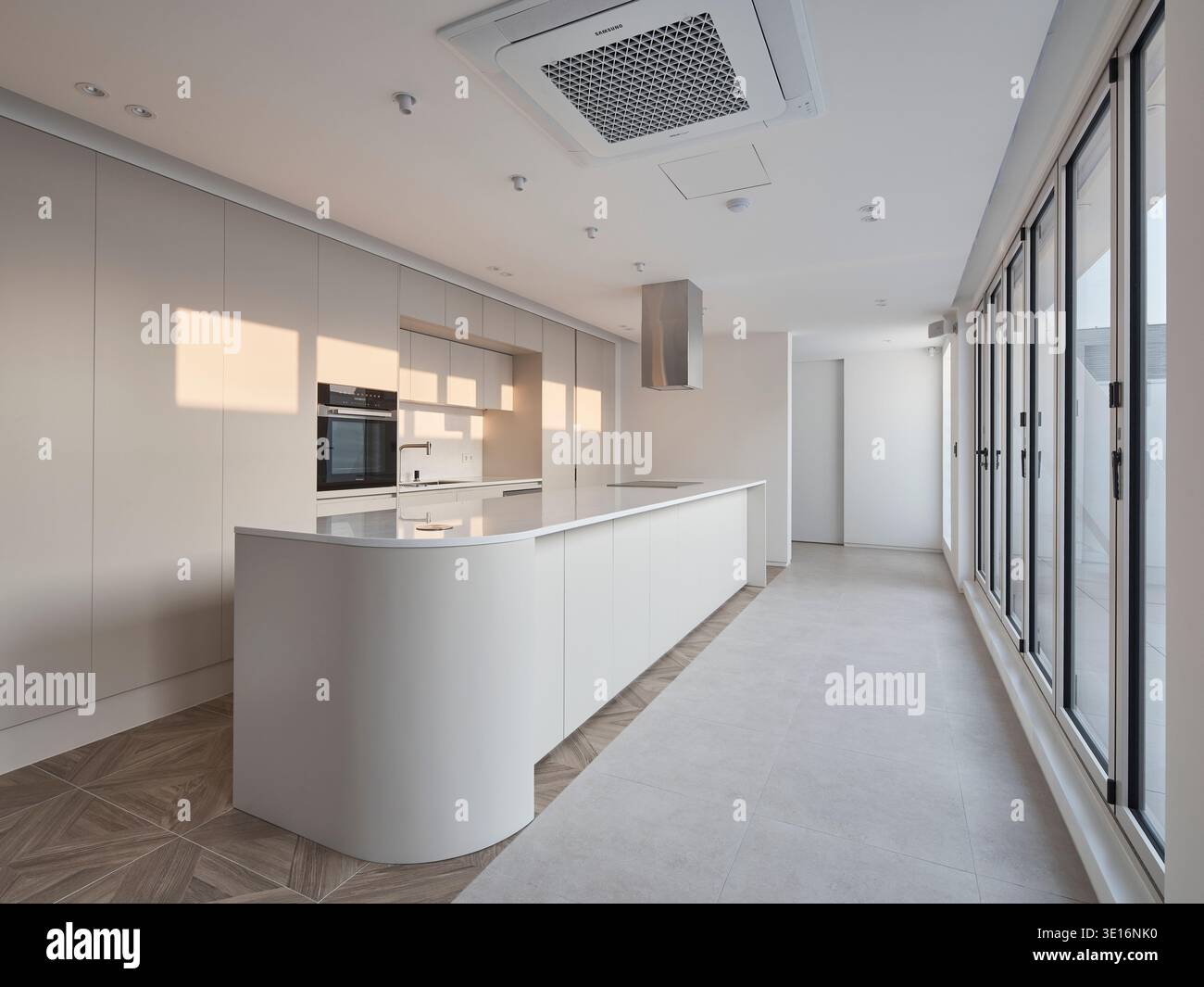 Weiße, minimalistische Küche mit großen Fenstern und weichem Tageslicht. Stockfoto