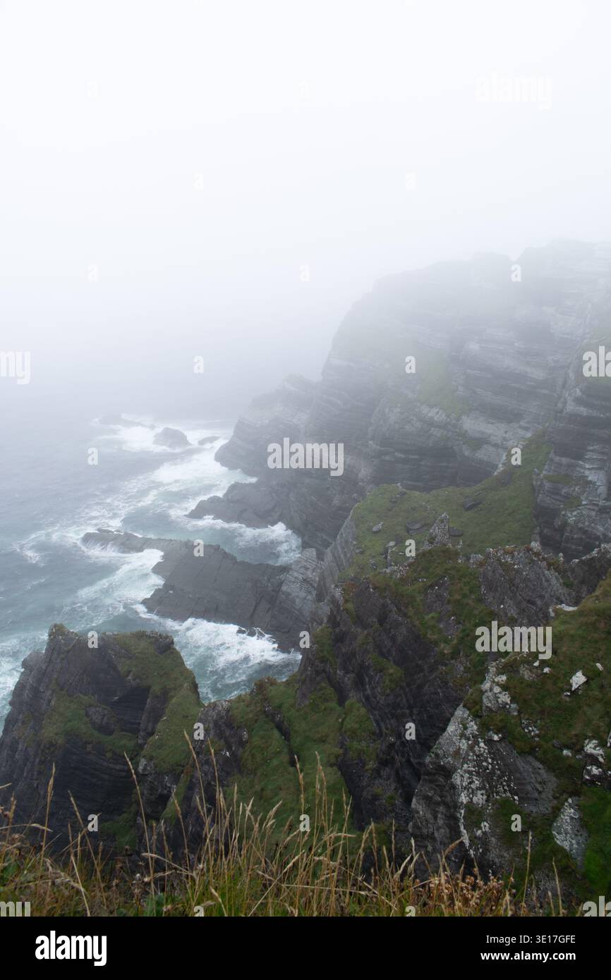 Ring of Kerry Klippen an einem nebeligen Tag mit vielen Wolken und Nebel. Scharfe Berge neben einem aufgewühlten Meer Stockfoto