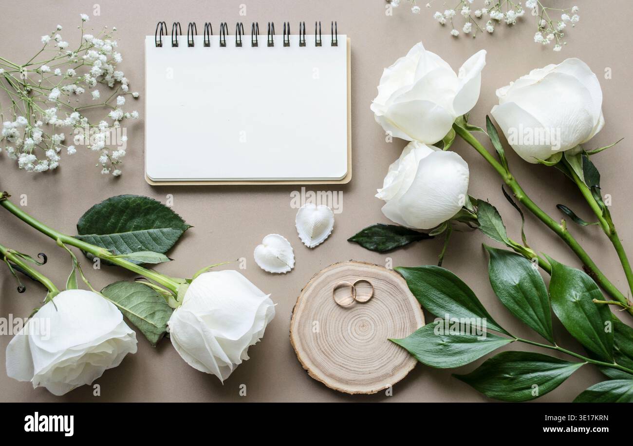 Romantisches Modell mit Blumen und einem Notizbuch auf beigefarbenem Hintergrund. Rosen und ein Notizbuch mit Platz für Text. Hochzeitskonzept. Blick von oben. Stockfoto