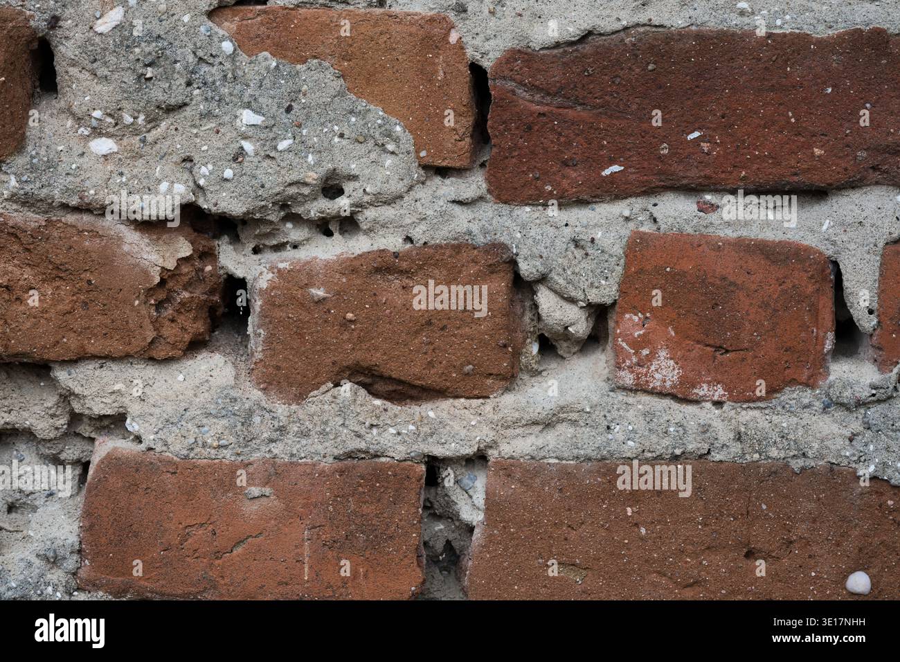 Makrostruktur einer alten roten Ziegelwand mit grauem Betonmörtel. Detailansicht der verwitterten und beschädigten Mauerwerksoberfläche mit sichtbaren Lücken Stockfoto
