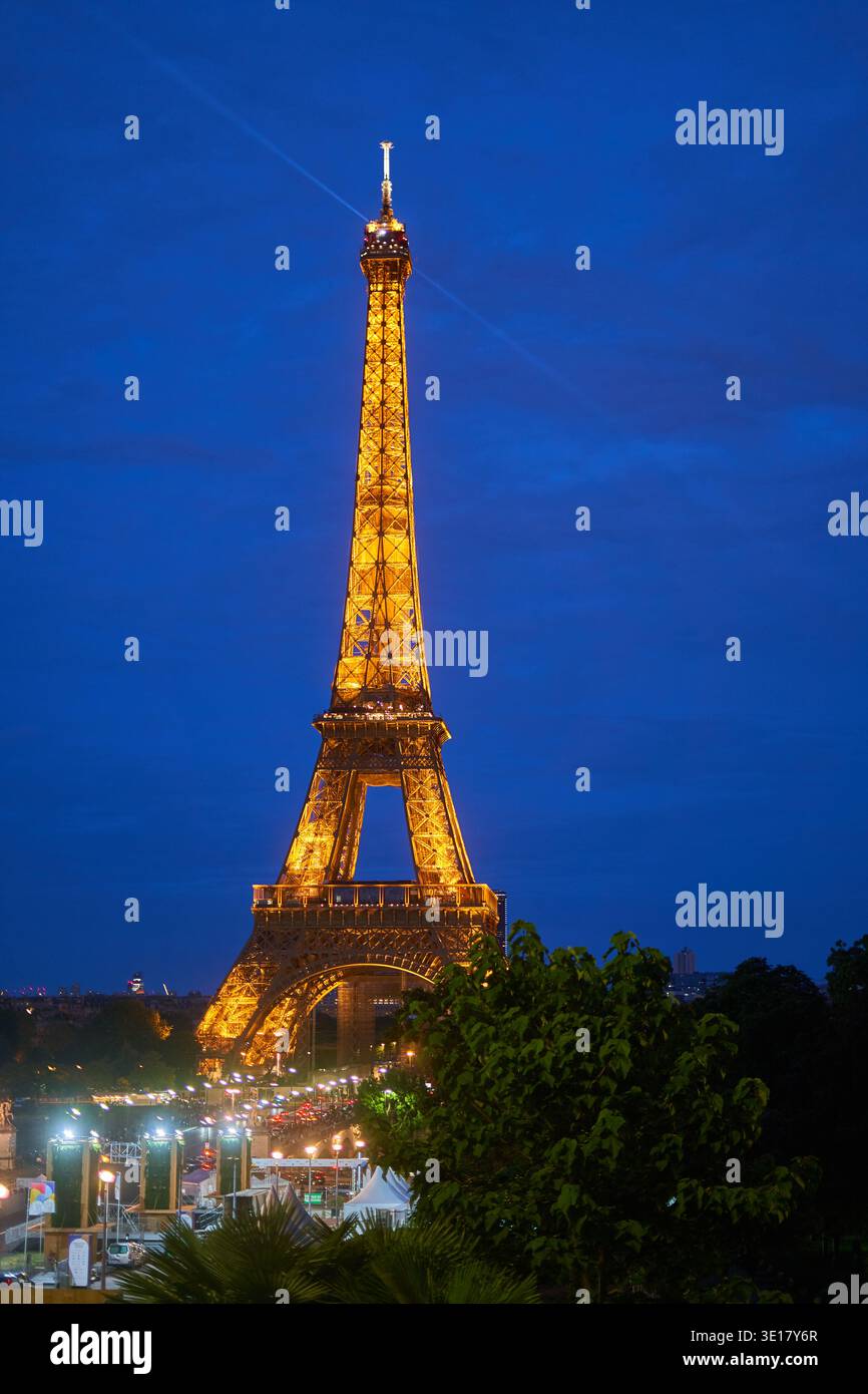 Der Eiffelturm steht majestätisch beleuchtet vor einem tiefblauen Abendhimmel in Paris, Frankreich. Die ikonische Eisengitterstruktur leuchtet mit... Stockfoto
