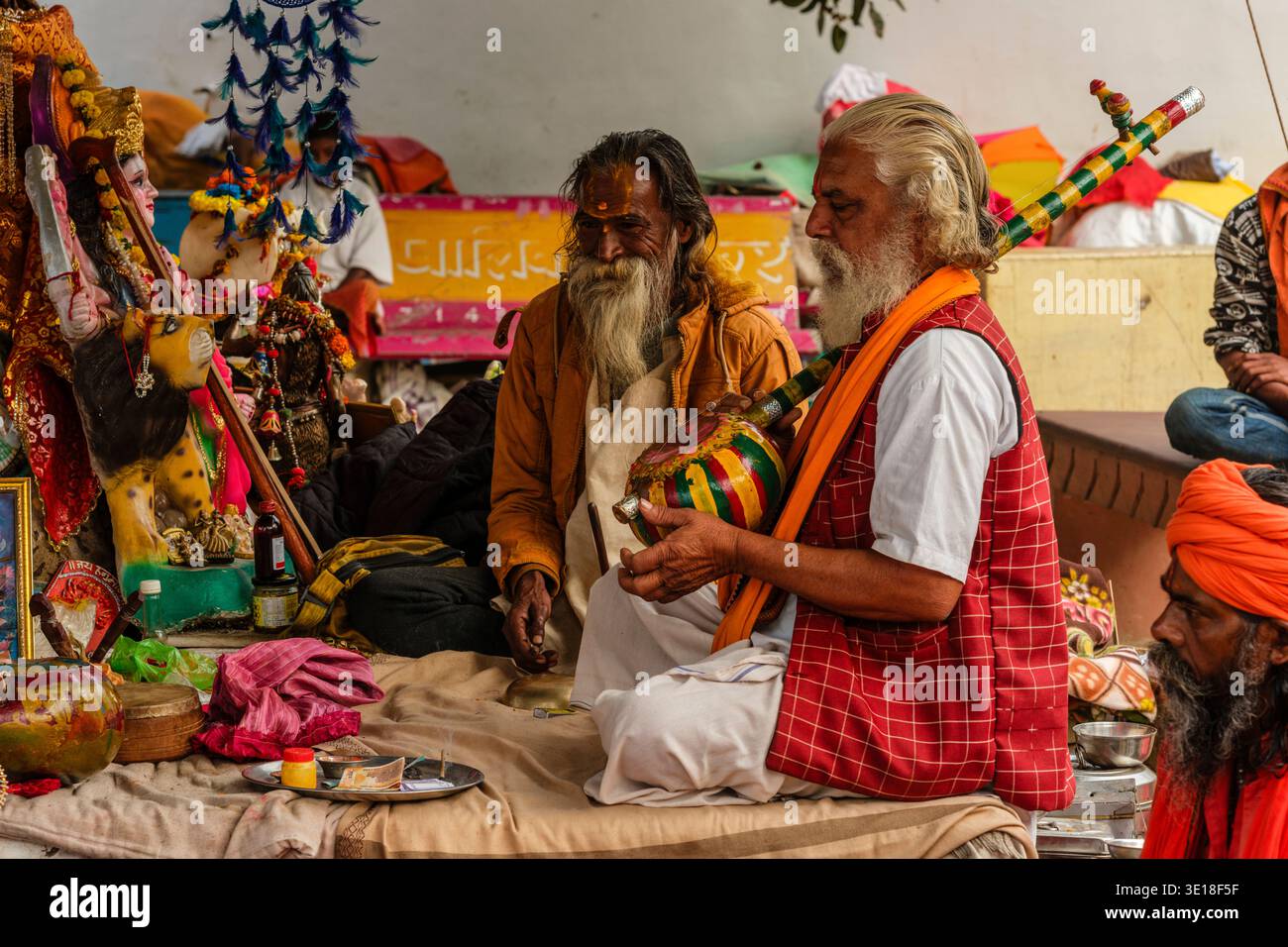 Sadhus, heilige Männer, sitzen im Sunset Ghat am Pushkar Lake, einer spielt ein Streifeninstrument, während Dekorationen in der Ferne hängen. Stockfoto