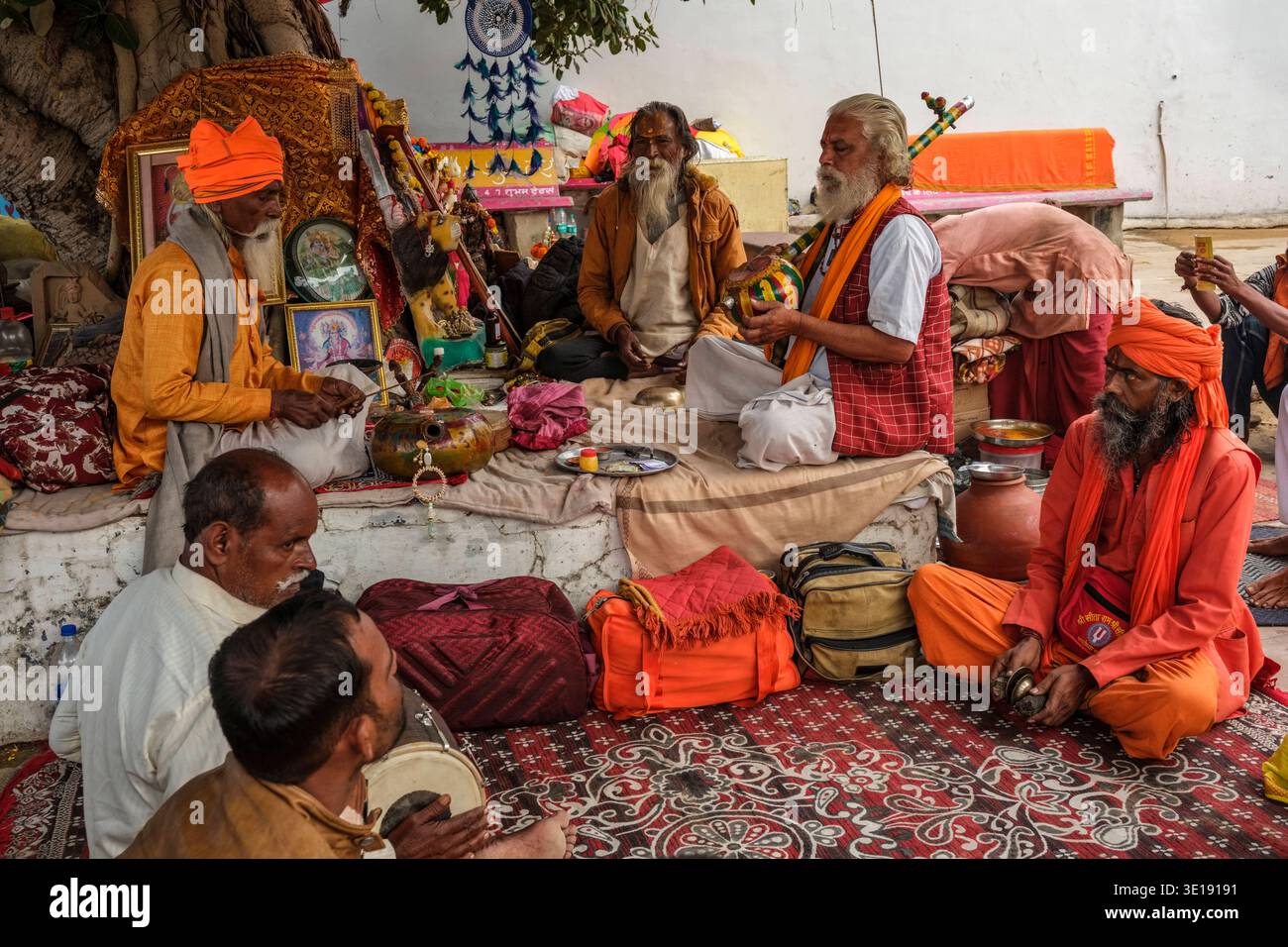 Sadhus, heilige Männer, versammeln sich auf einem Teppich am Sunset Ghat am Pushkar Lake, um Musik zu spielen und Rituale zu führen, umgeben von Taschen und religiösen Opfergaben. Puschkar Stockfoto